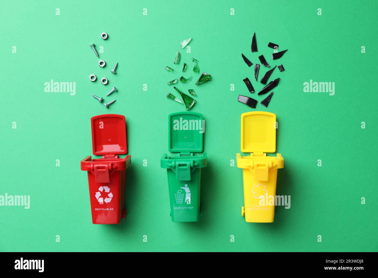Mini recycling bins and different garbage on green background, flat lay