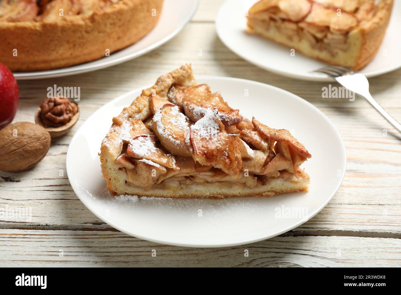 Slice of delicious apple pie with powdered sugar served on white wooden table Stock Photo
