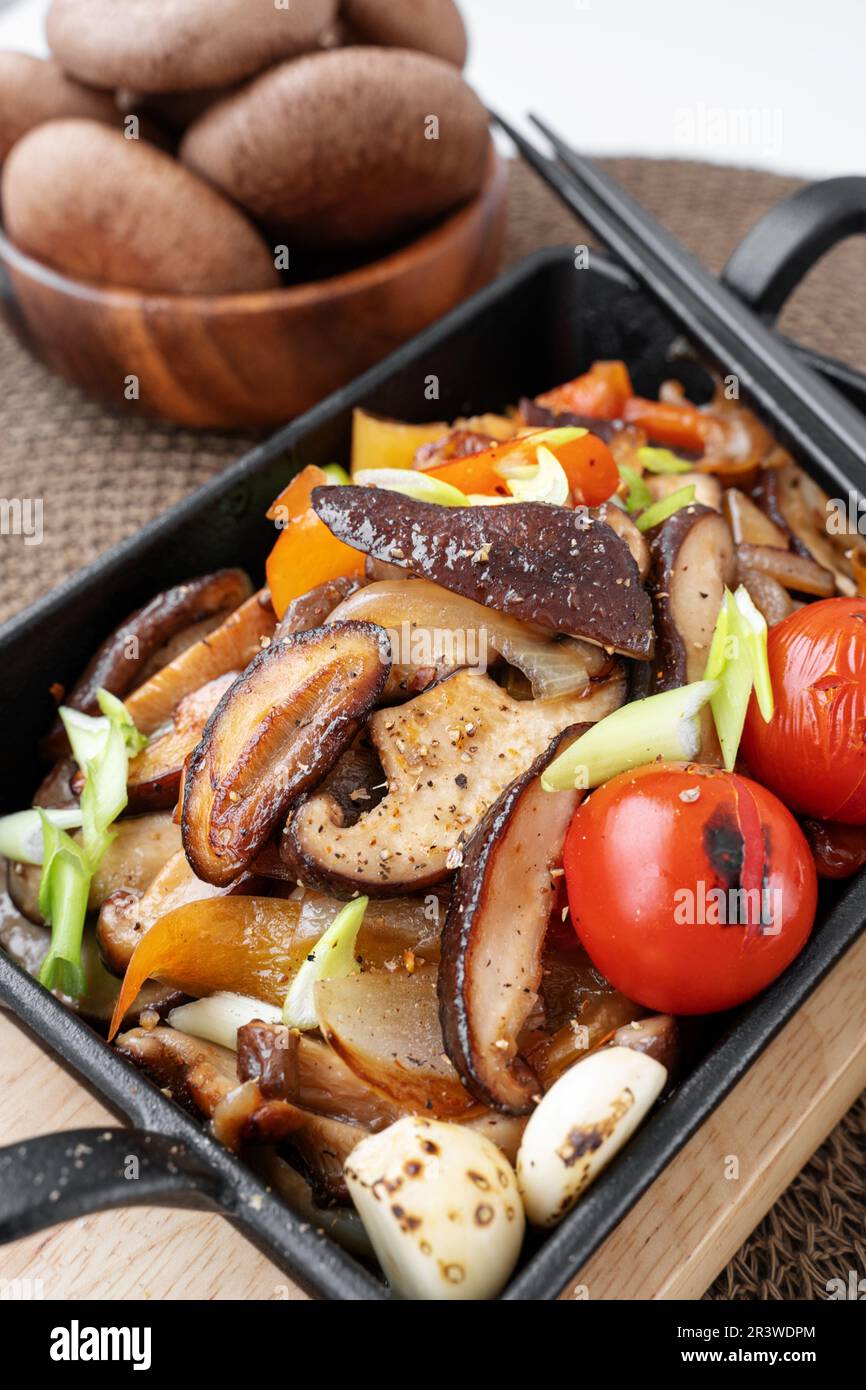 Fried shiitake mushrooms with vegetables, bell peppers, onions and tomatoes are ready for consumption. Vegetable vegetarian dish with shiitake mushroo Stock Photo