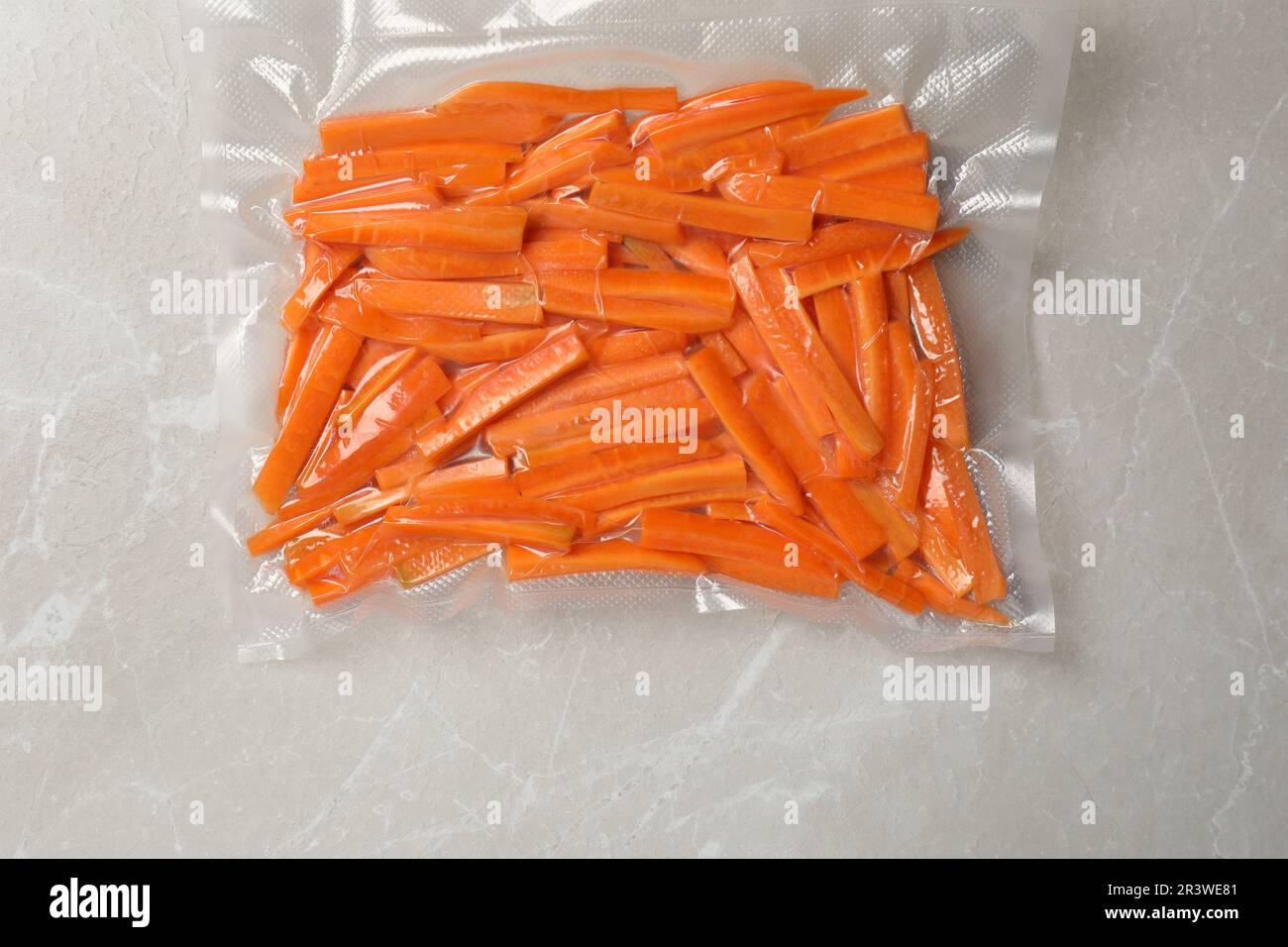 Vacuum packing with cut carrots on light grey marble table, top view