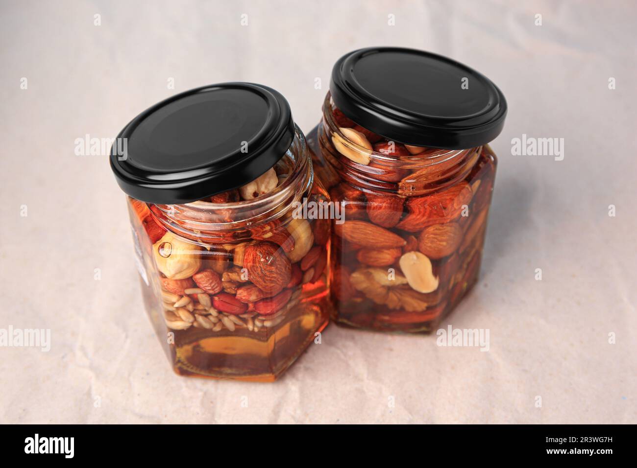 Jars with different nuts and honey on beige background Stock Photo