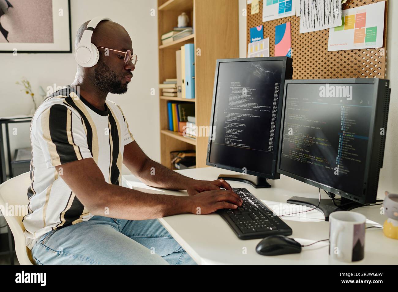 African American programmer in wireless headphones developing computer codes on computer sitting at his workplace in office Stock Photo