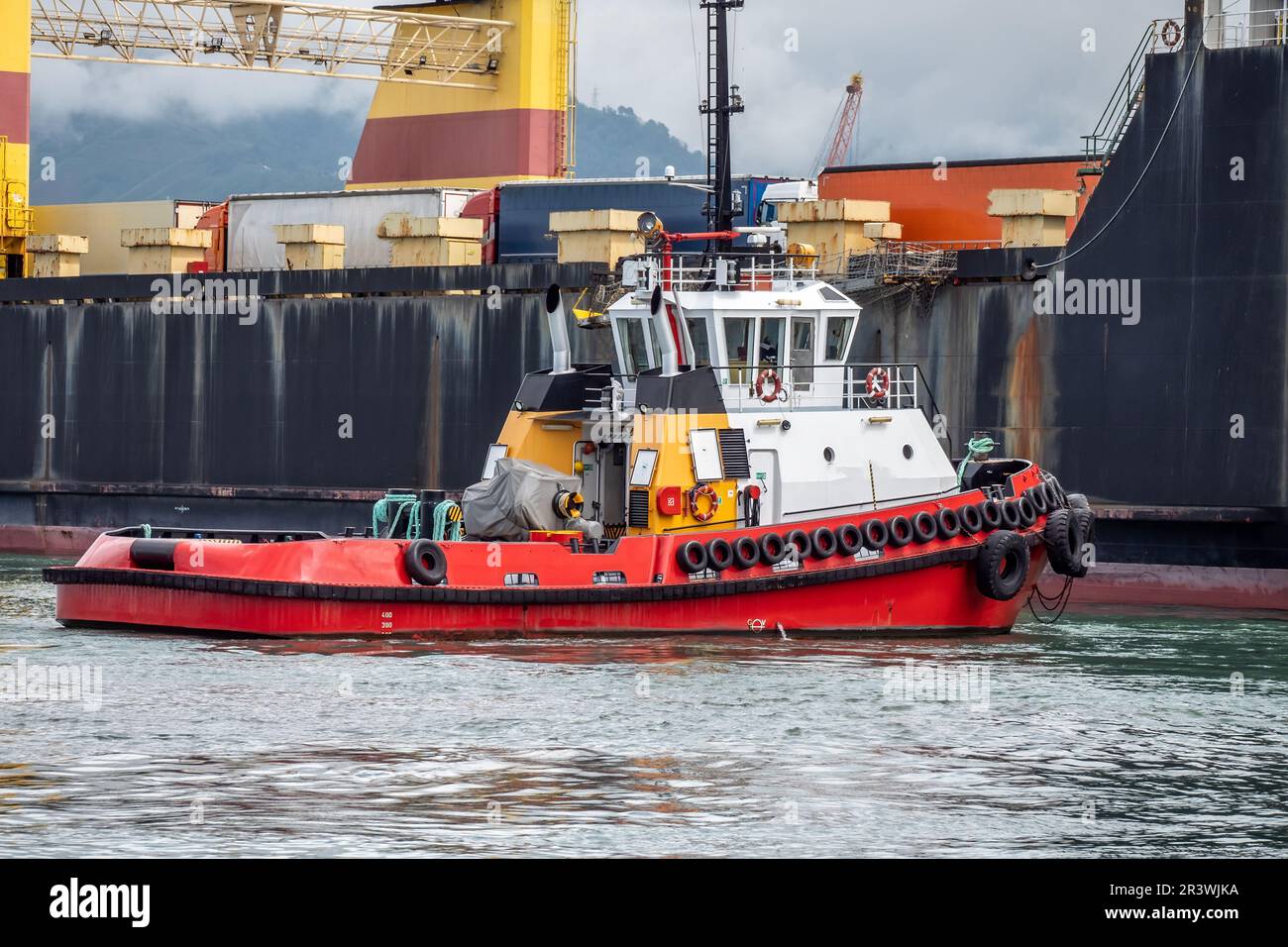 Tugboat push large cargo ship that has arrived at port dock. Freight sea transportation concept. Stock Photo
