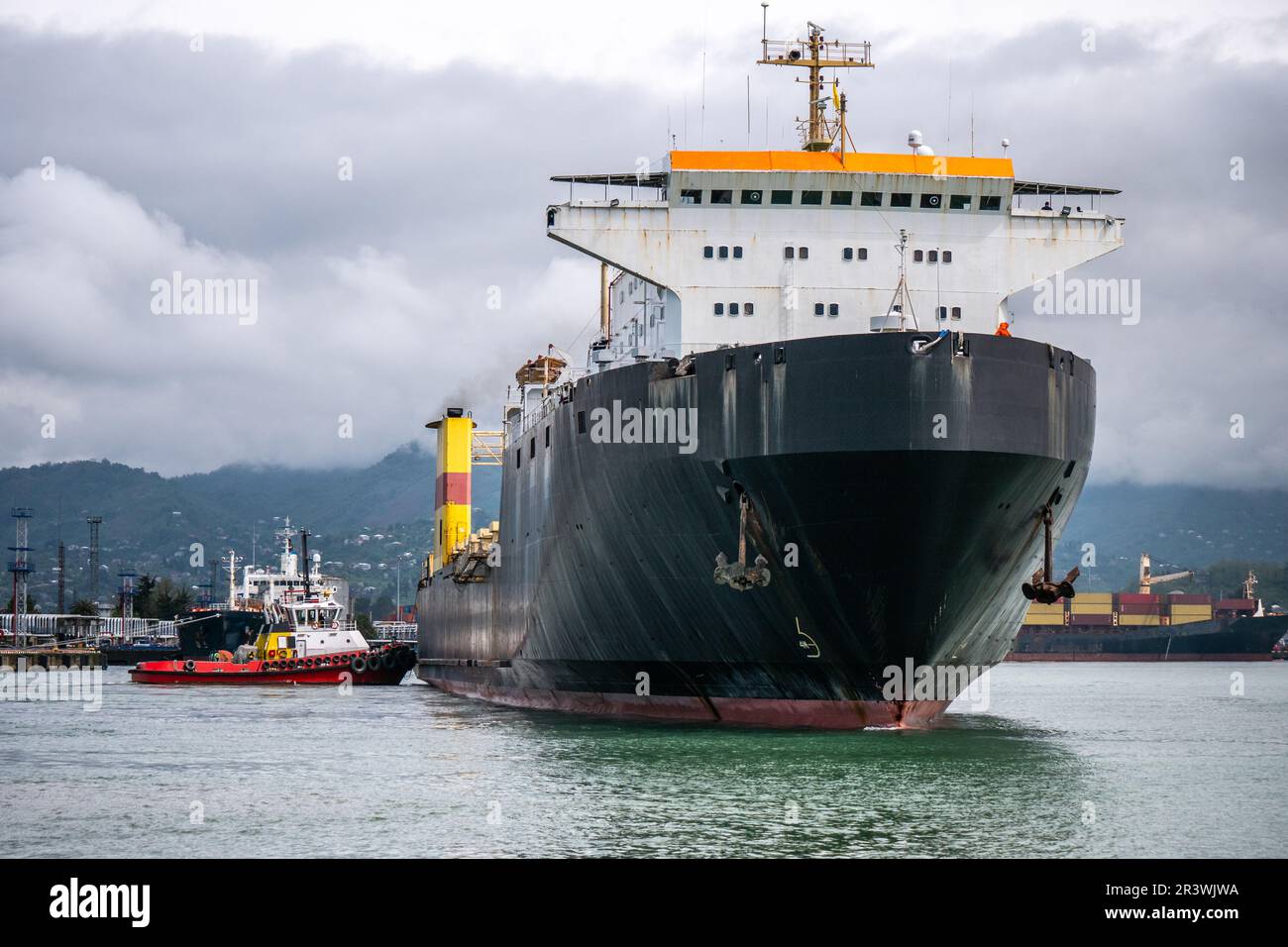 Tugboat push large cargo ship that has arrived at port dock. Freight sea transportation concept. Stock Photo