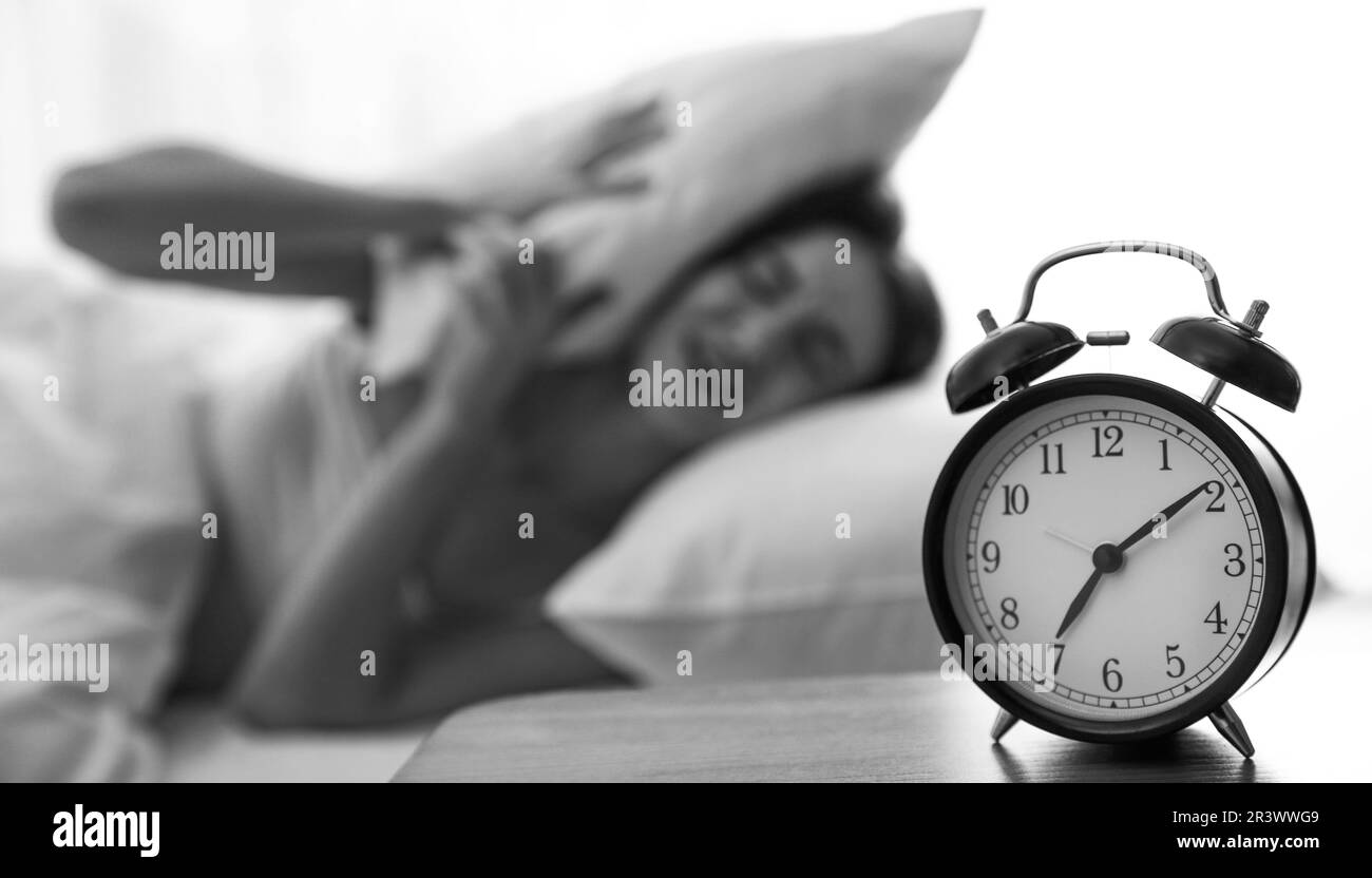 Young woman covering ears with pillow at home in morning, selective focus. Black and white photography Stock Photo