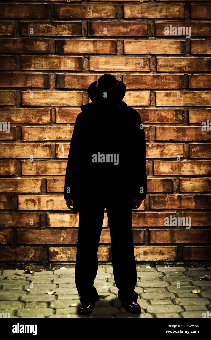 man in front of a bricks wall, wearing a fedora hat and hiding his face Stock Photo