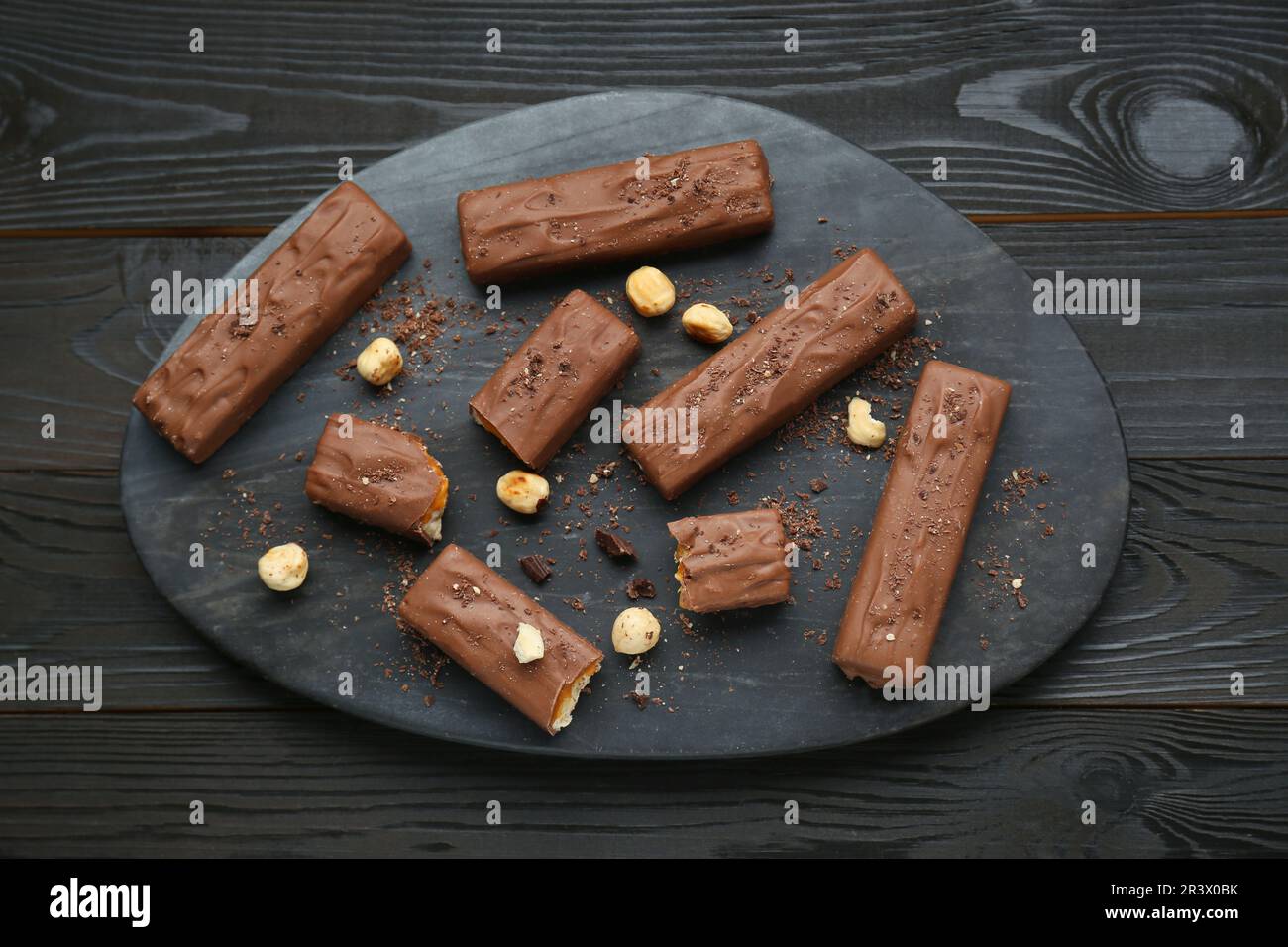 Board with delicious chocolate bars and nuts on black wooden table, top ...