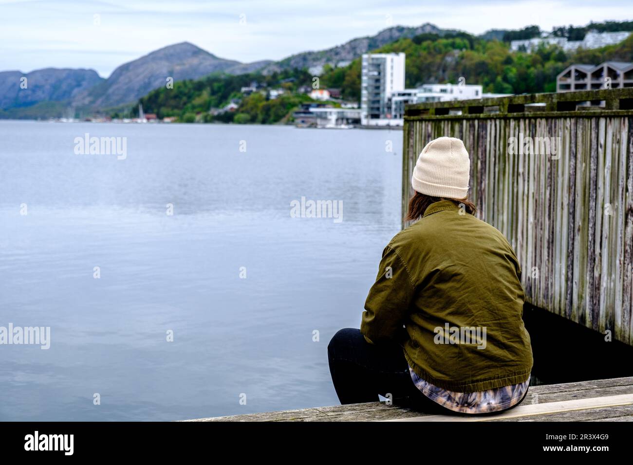 Sandnes, Norway, May 18 2023, Man Alone Sitting On Dock With Back To Camera Looking Out To Sea Stock Photo