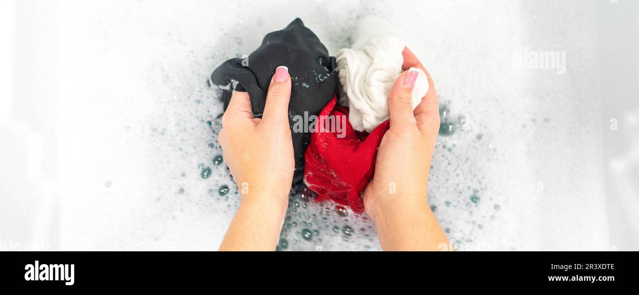 Panorama of female hands washing black, red and white clothes in white foam Stock Photo