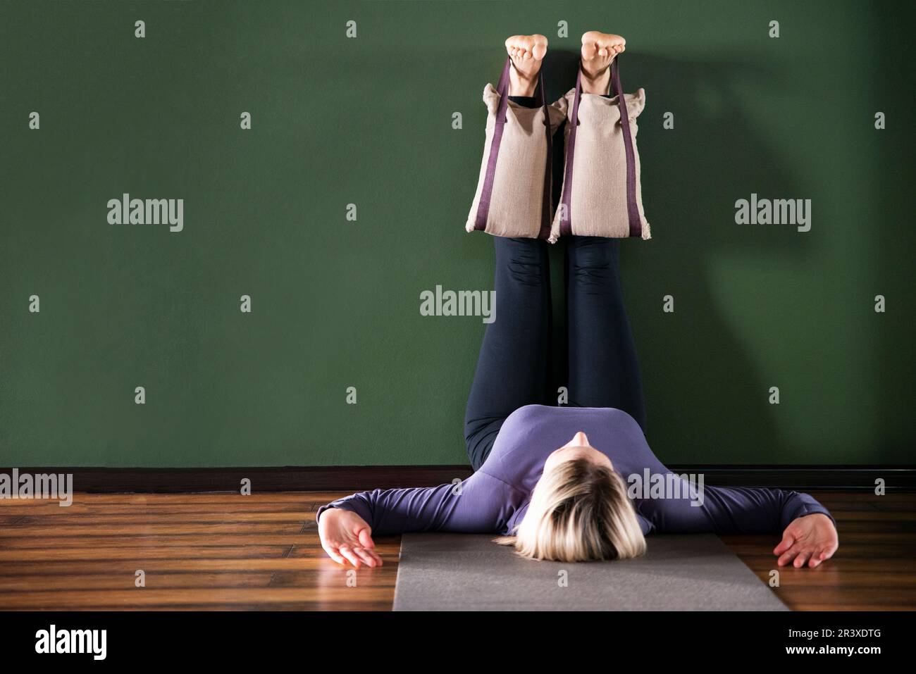 Young woman in yoga relaxing pose with legs up against wall with heavy