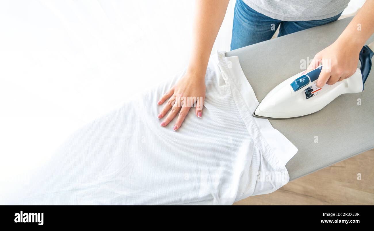 Female hands ironing white shirt collar on ironing board, view from