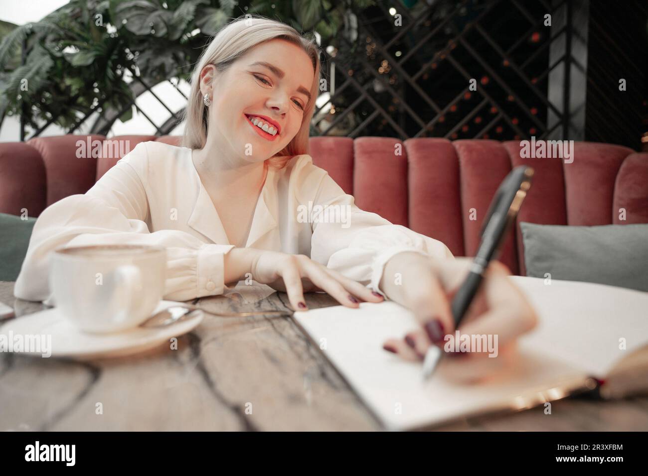 Girl writing down future plans and goals in own diary resting in cozy cafeteria Stock Photo