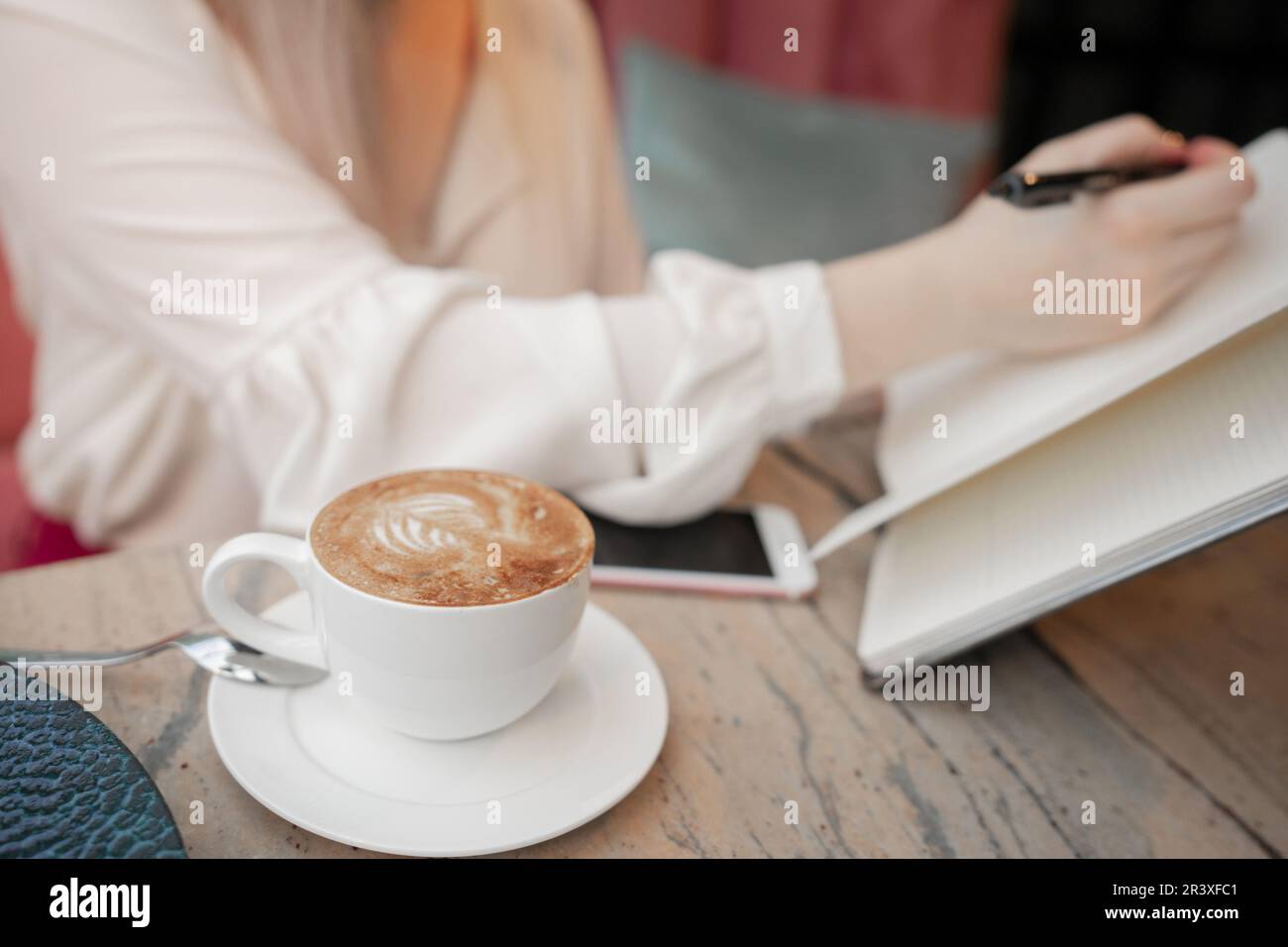 Cropped image of girl making notes in open notepad while drinking coffee Stock Photo