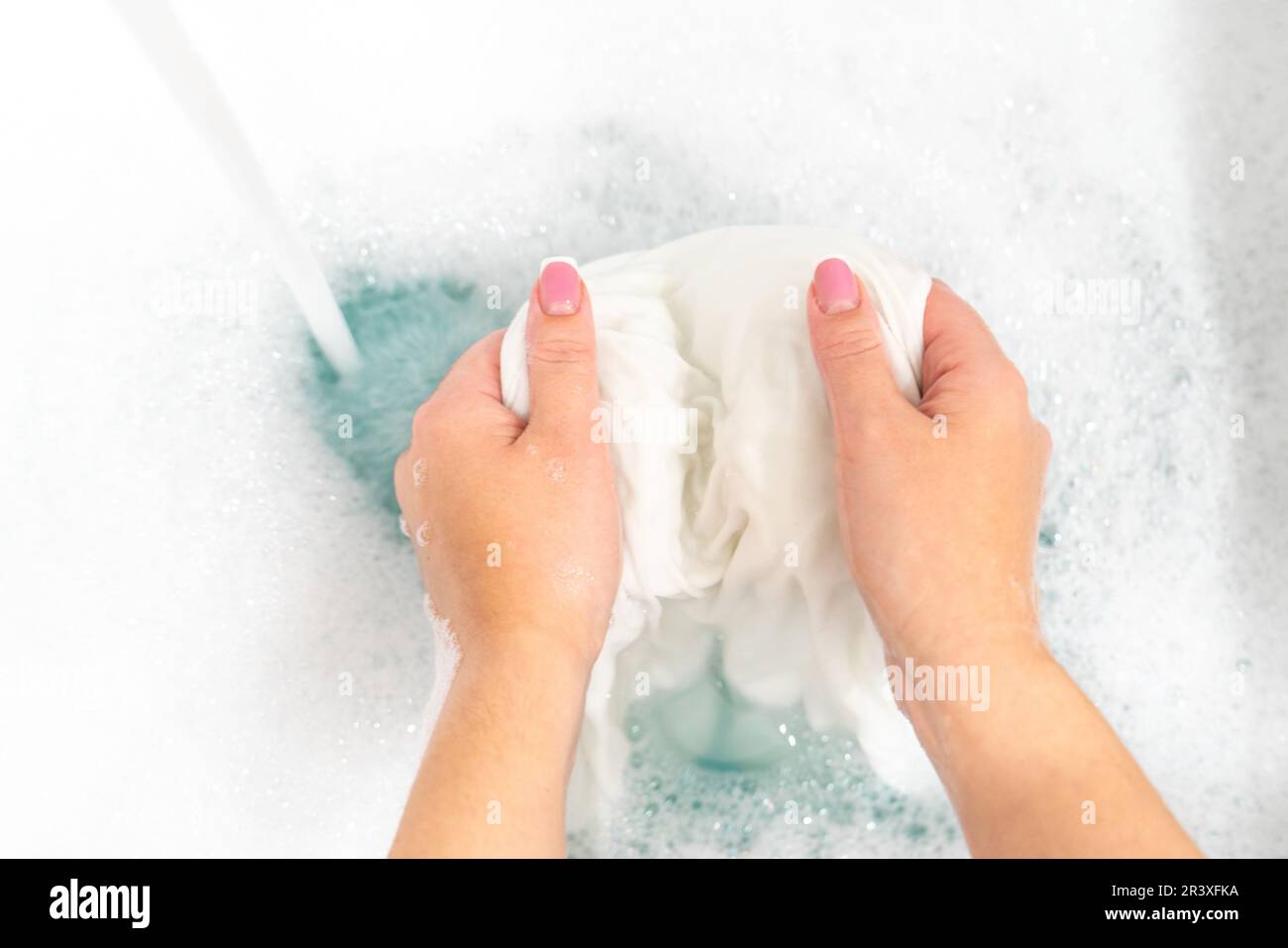 Wash clothing by hand with whitening detergent in laundry sink Stock