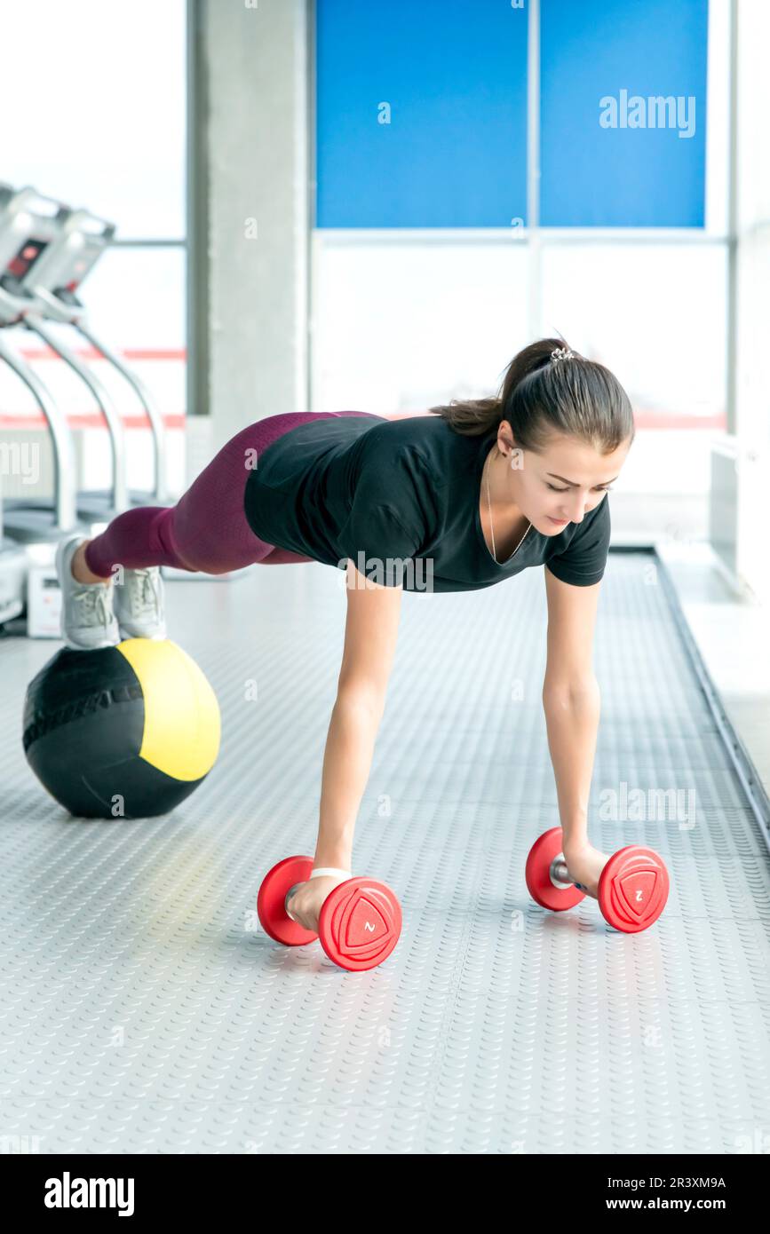 Fitness girl doing dumbbells and medicine ball plank. Woman doing floor