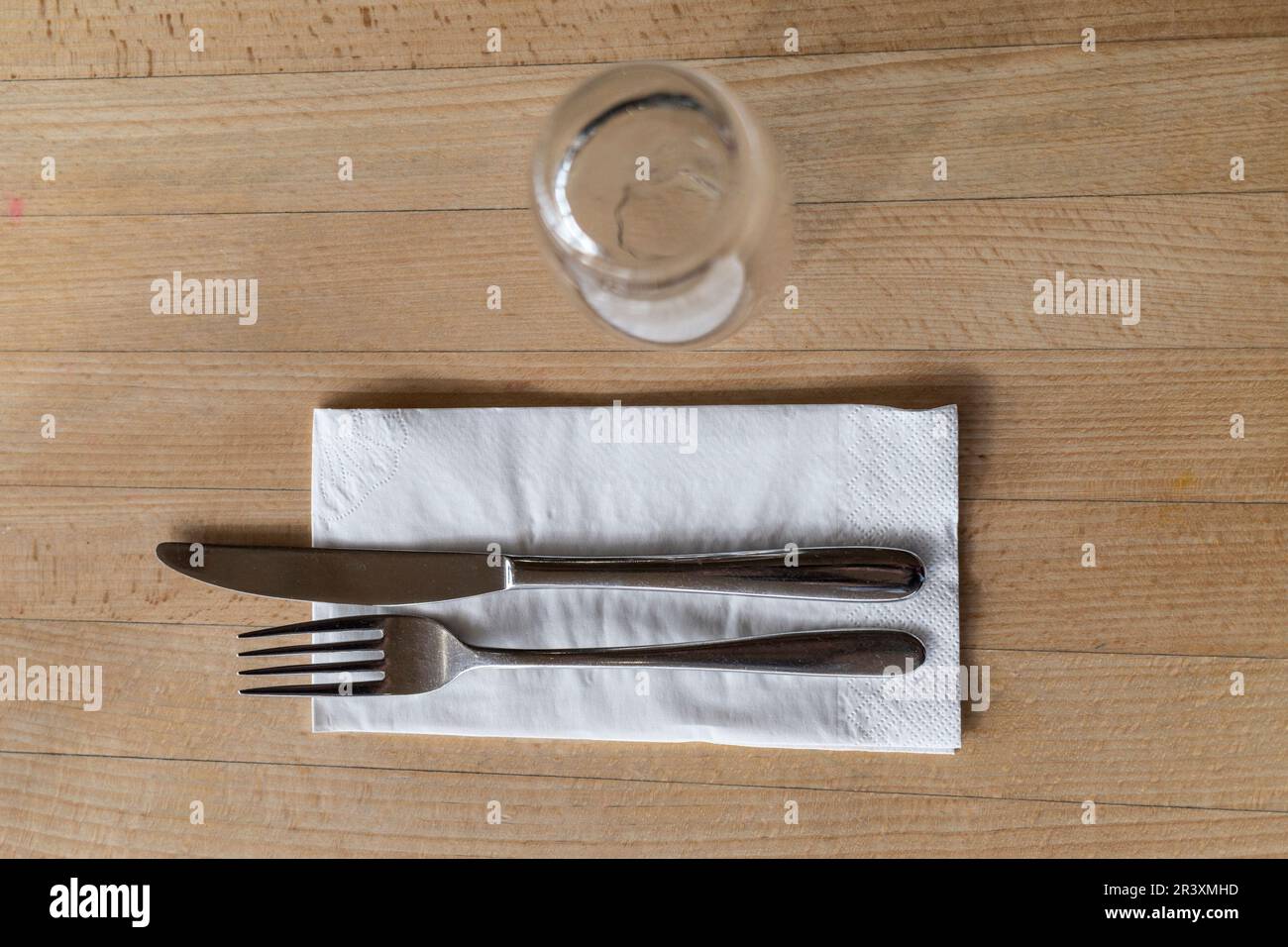 A knife and fork placed on a paper napkin serviette on a table. Stock Photo