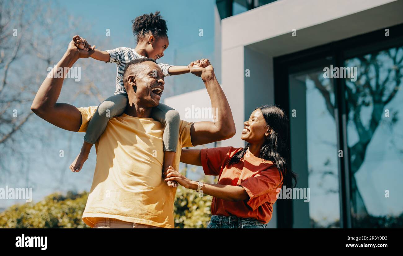 Family fun time with mom and dad at home. Couple playing with their daughter and creating happy childhood memories. Dad carrying his daughter on his s Stock Photo