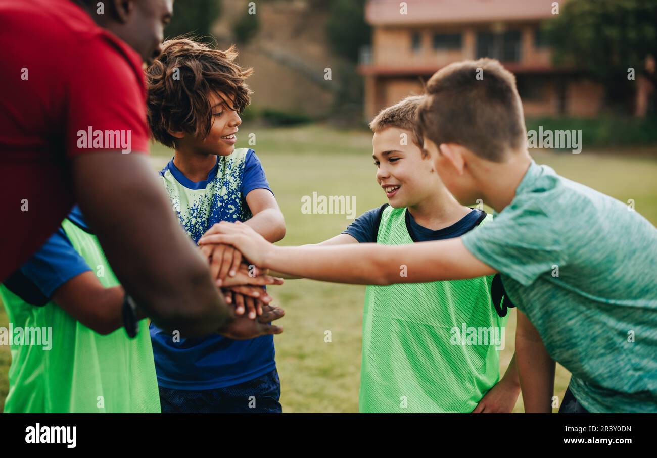 school kids having a huddle with their coach in a sports field. Rugby team having a motivational pep talk before practice. Sports coach mentoring chil Stock Photo