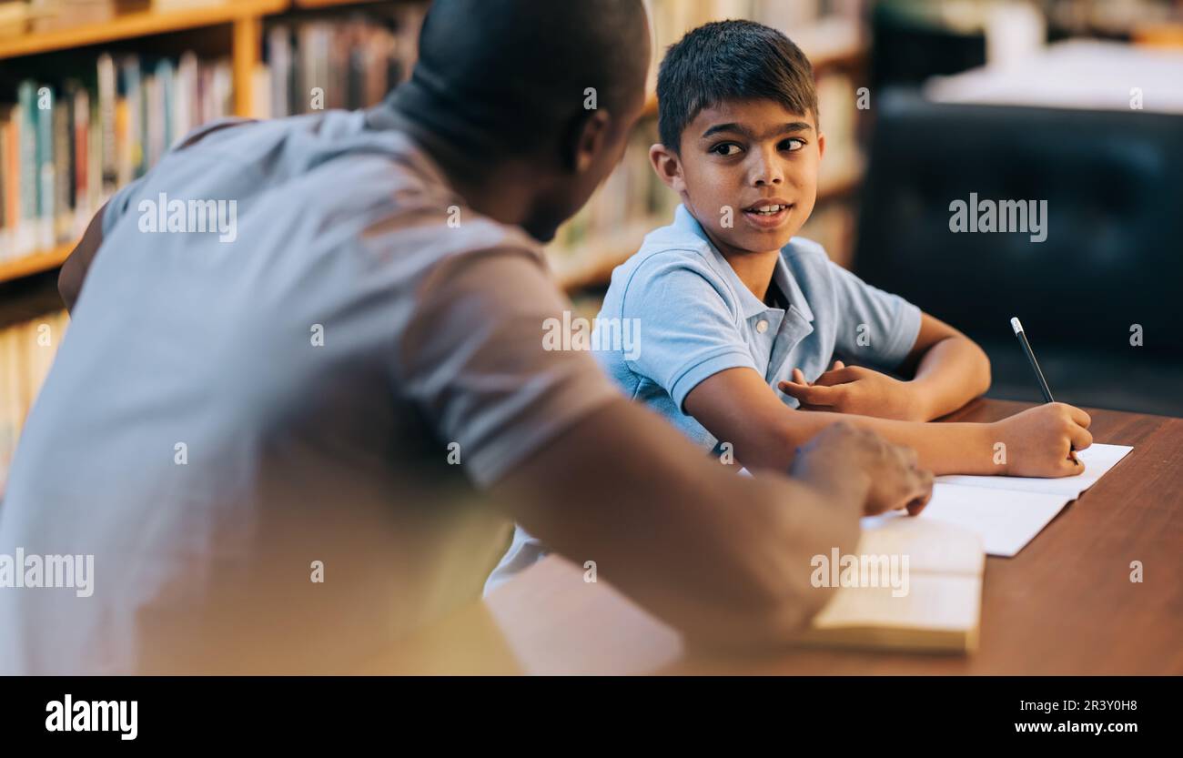 Tutoring and academic support in primary school. Young school boy talking to his teacher during a private lesson in a library. Elementary school stude Stock Photo
