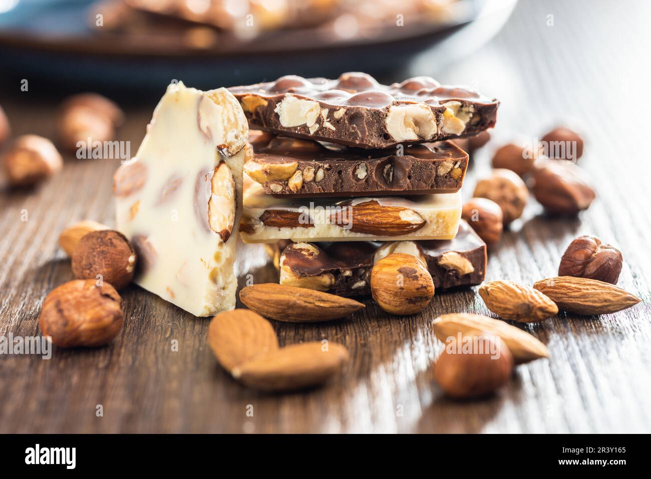 Broken chocolate bars with nuts on the wooden table. Stock Photo