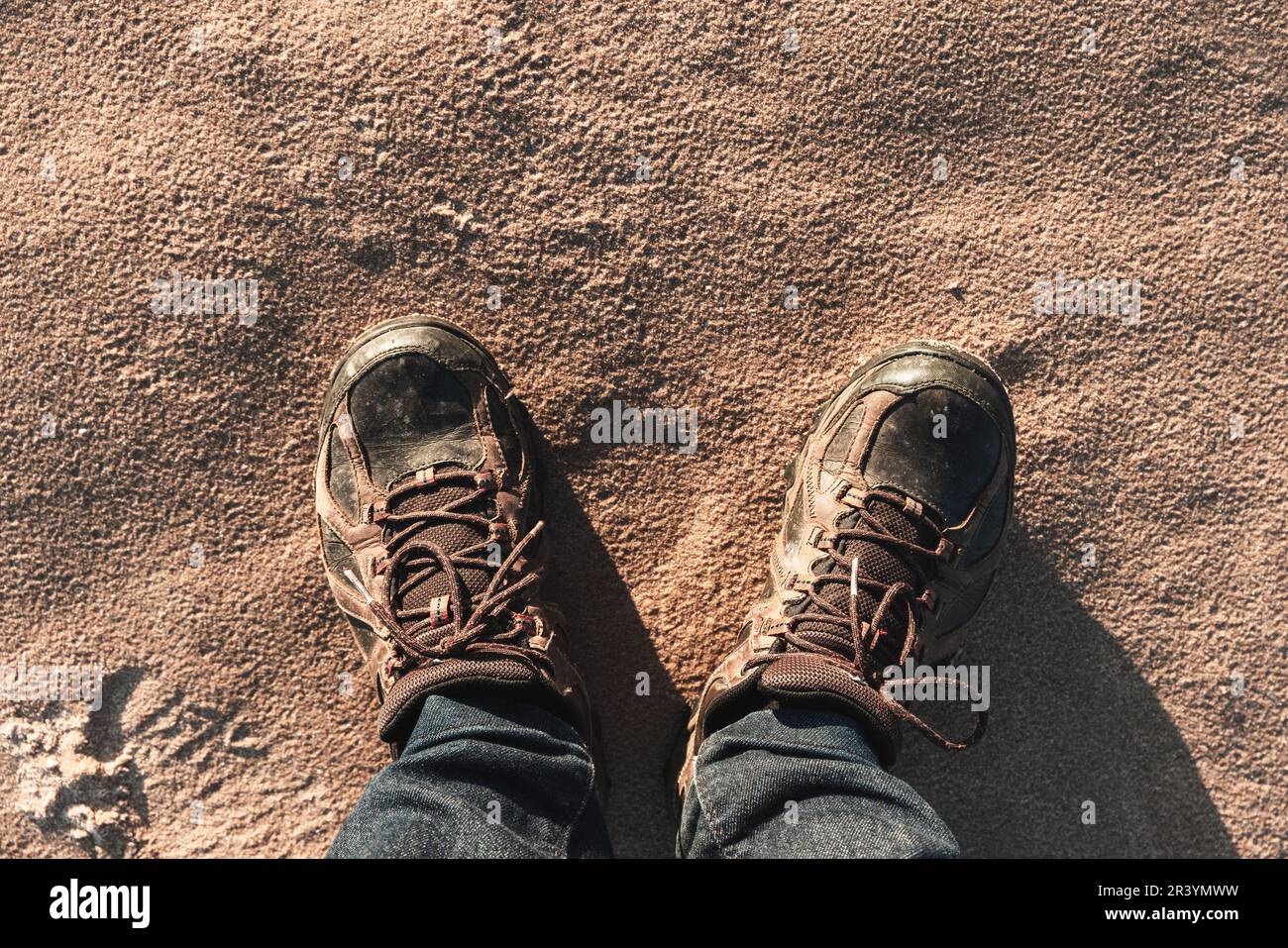 Male feet in trekking boots standing on sandy beach ground, first
