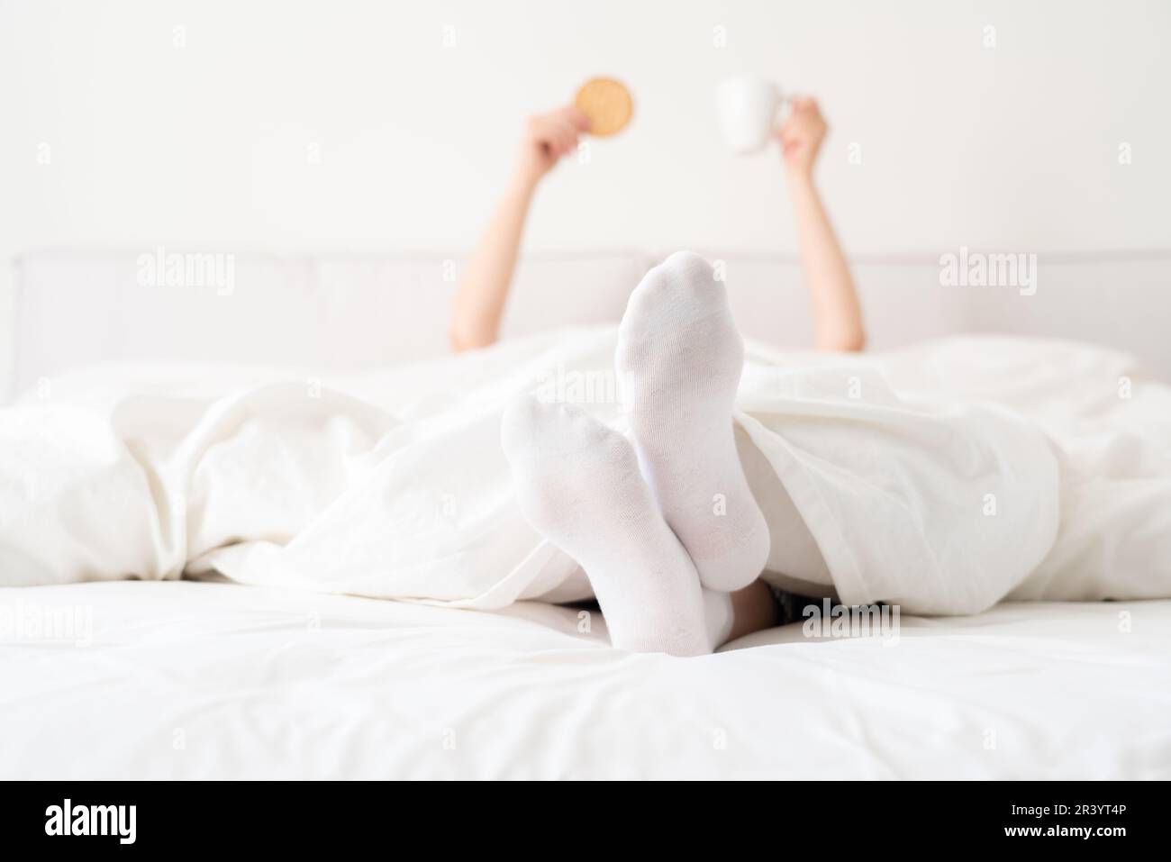 Female feet wearing white socks under blanket in bed. Woman waking up in the morning Stock Photo