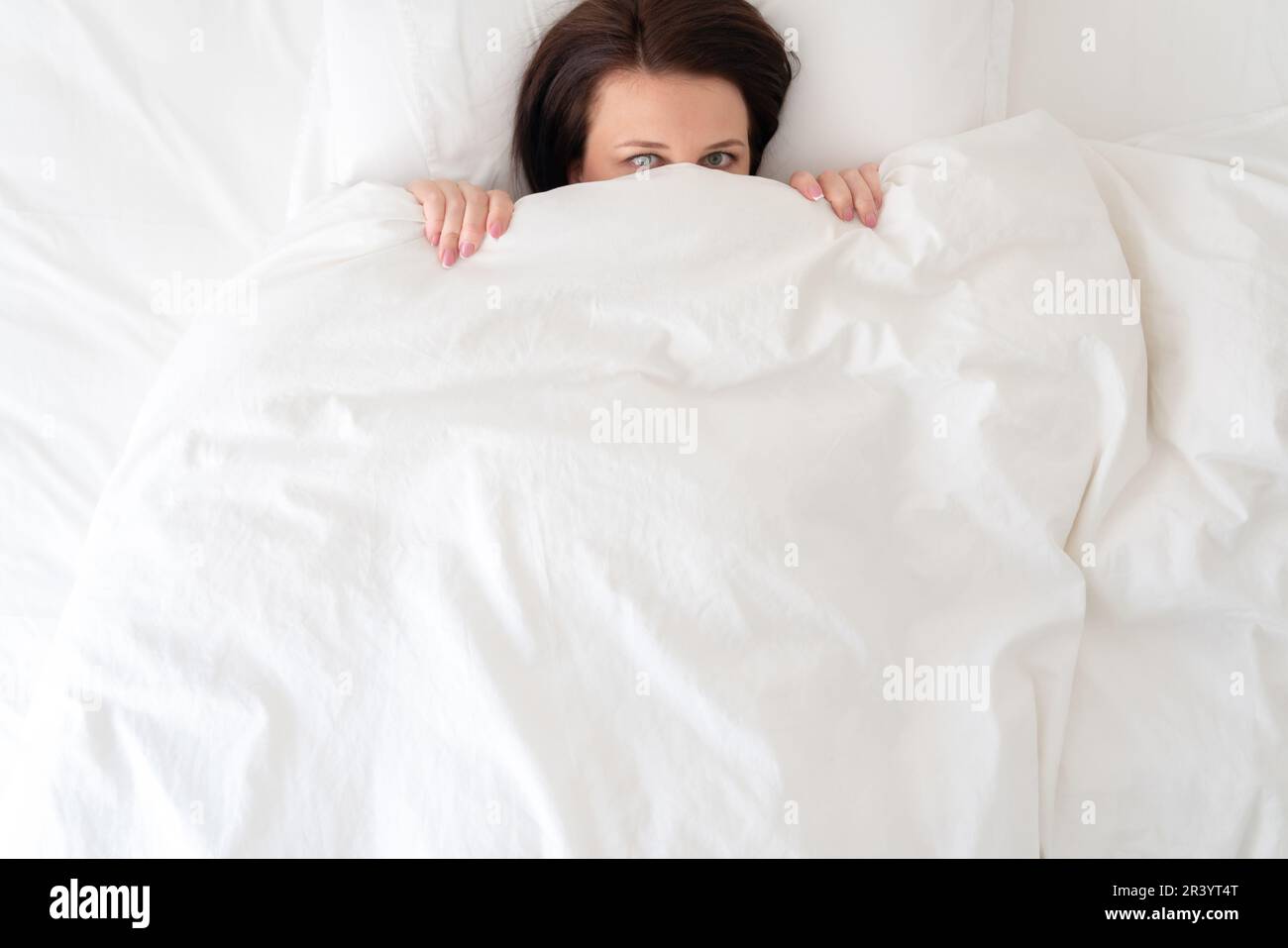 Young beautiful woman in bed hiding under duvet Stock Photo
