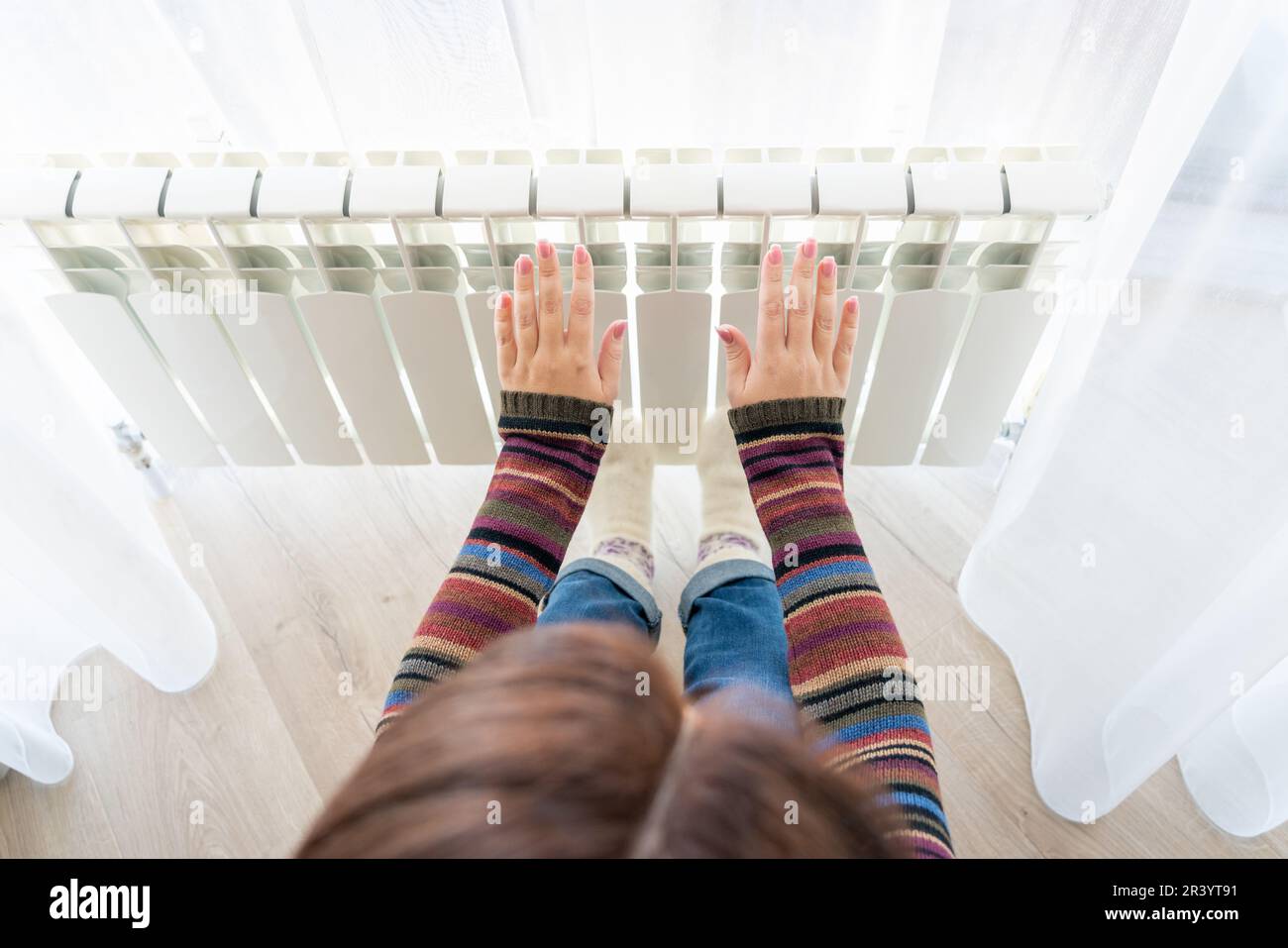 Girl warms up the frozen hands above hot radiator, close up view Stock Photo