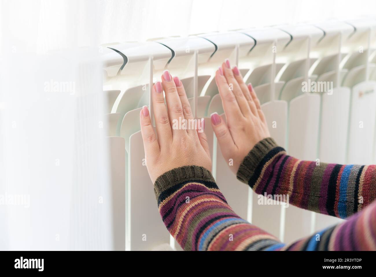 Girl warms up the frozen hands above hot radiator, close up view Stock Photo