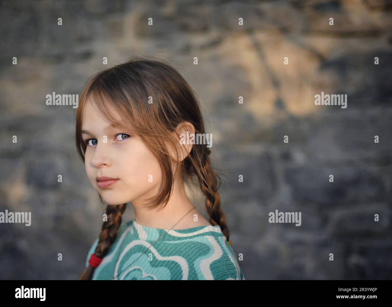 Beautiful young blonde little girl wearing pigtail hairstyle posing with stone brick wall in the background Stock Photo