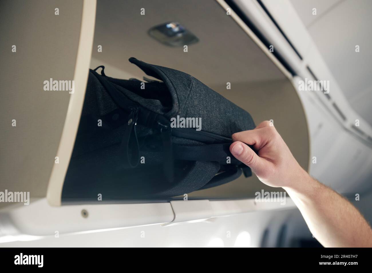 Man travel by plane. Close-up hand of passenger is putting hand baggage in lockers above airplane seats. Stock Photo