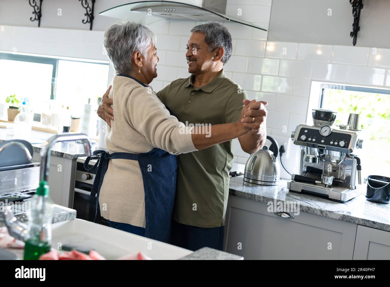 Happy biracial senior couple holding hands and looking at each other while dancing in kitchen Stock Photo