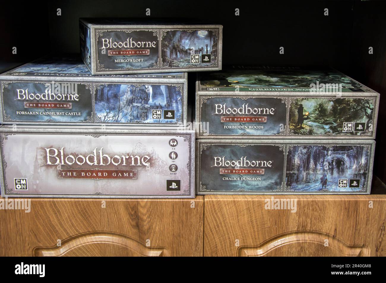 A collection of Bloodborne board games, five boxes - a core game and several expansions on a shelf. Stock Photo