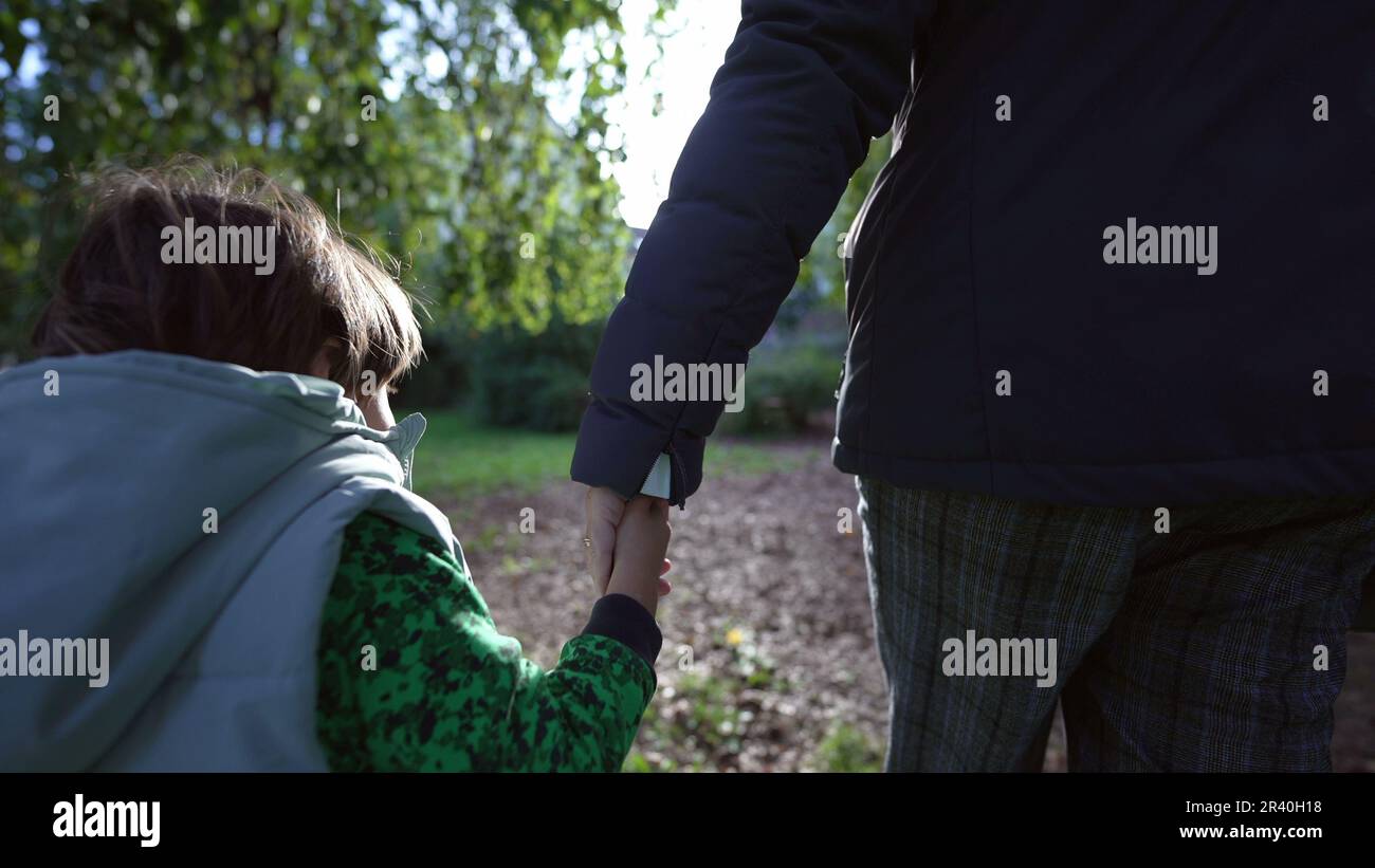 Mother and child holding hands walking outside at park during autumn ...