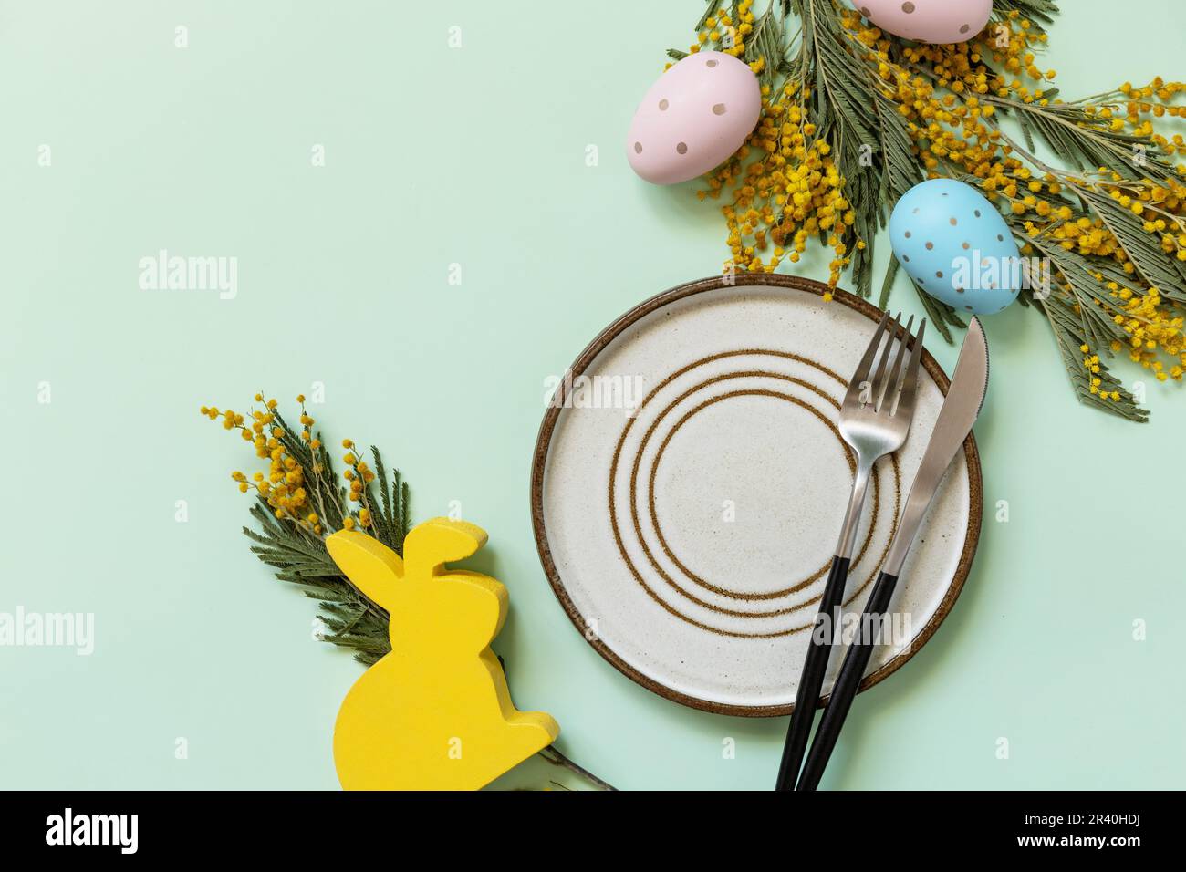 Easter table setting. Plate with easter eggs and mimosa on a pastel green background. Happy Easter holiday concept for restauran Stock Photo