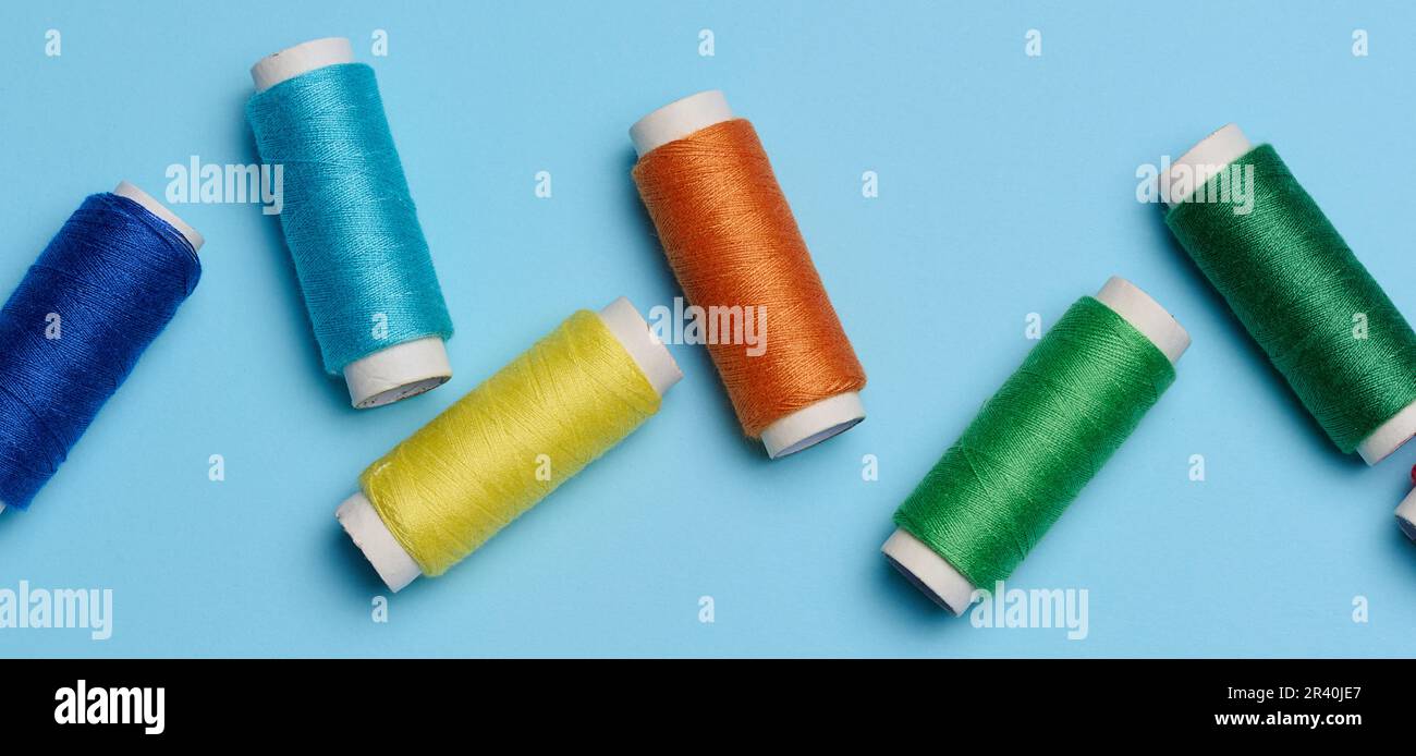 Multicolored spools of sewing threads on a blue background, top view Stock Photo
