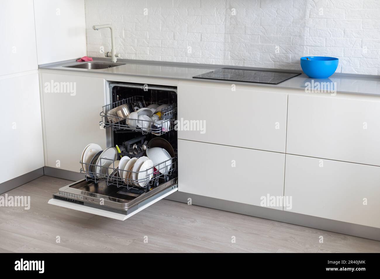 White kitchen counter and opened empty dishwasher wit grey
