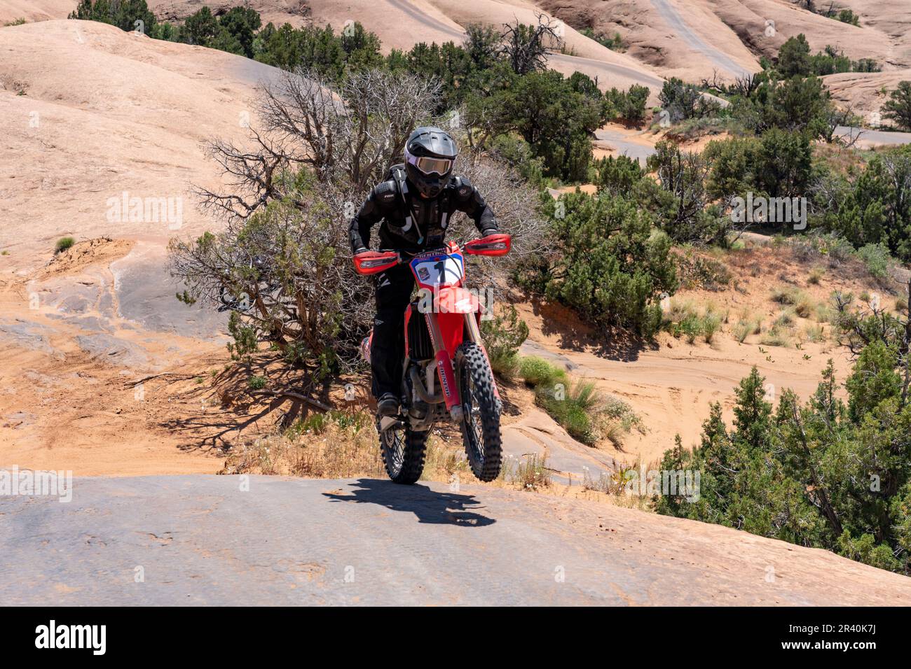 Off road motorcycle does a wheelie while climbing a sandstone dome of