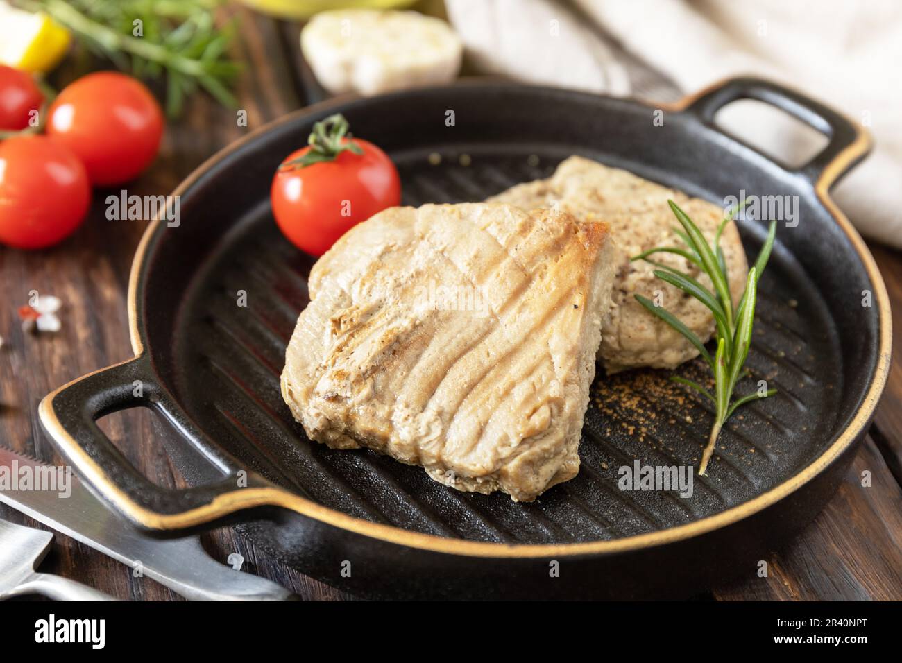 Restaurant food. Seafood. Rustic style. Cooked juicy tuna steak  with spices, tomatoes and rosemary on a stone plate. Stock Photo