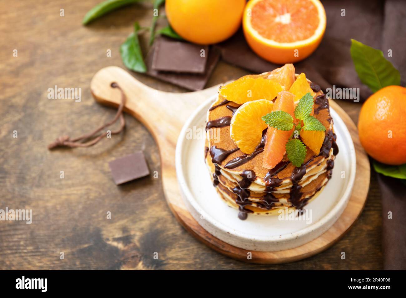 Celebrating Pancake day, healthy american breakfast. Delicious bananas pancakes with chocolate and red oranges on rustic table. Stock Photo