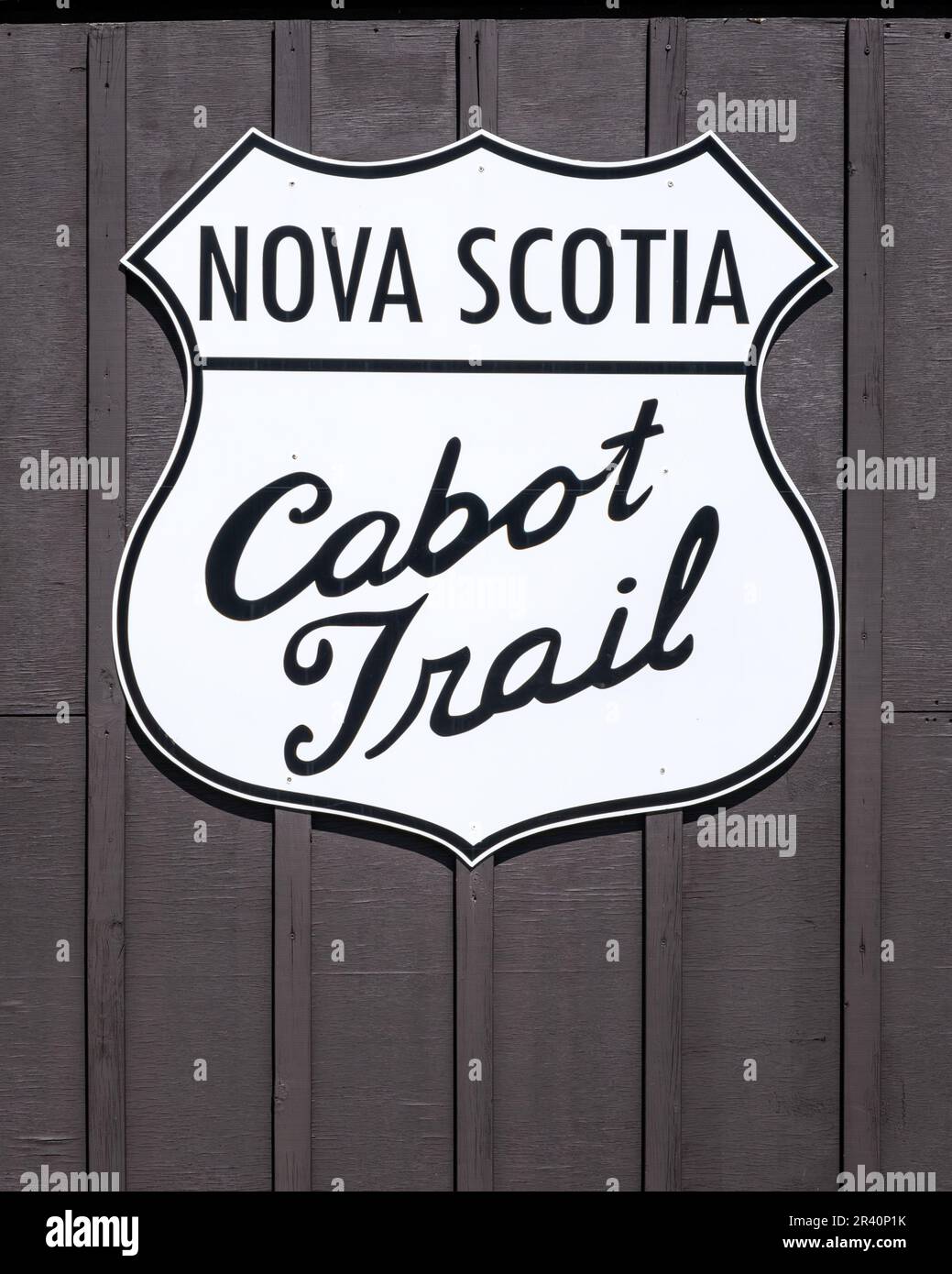 White Cabot Trail sign with blck script mounted on a brown wood background.  The Cabot Trail is the premier tourist attraction in Nova Scotia enjoyed Stock Photo