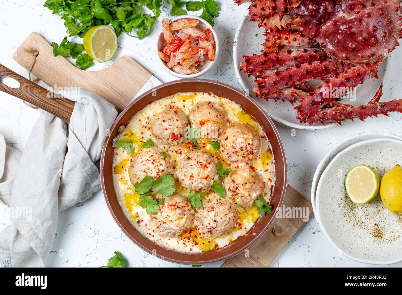 CRABMEATBALLS crab meatballs in white creamy sauce in red pan, whole king crab, cilantro, lemon and white wine on white backgrou Stock Photo