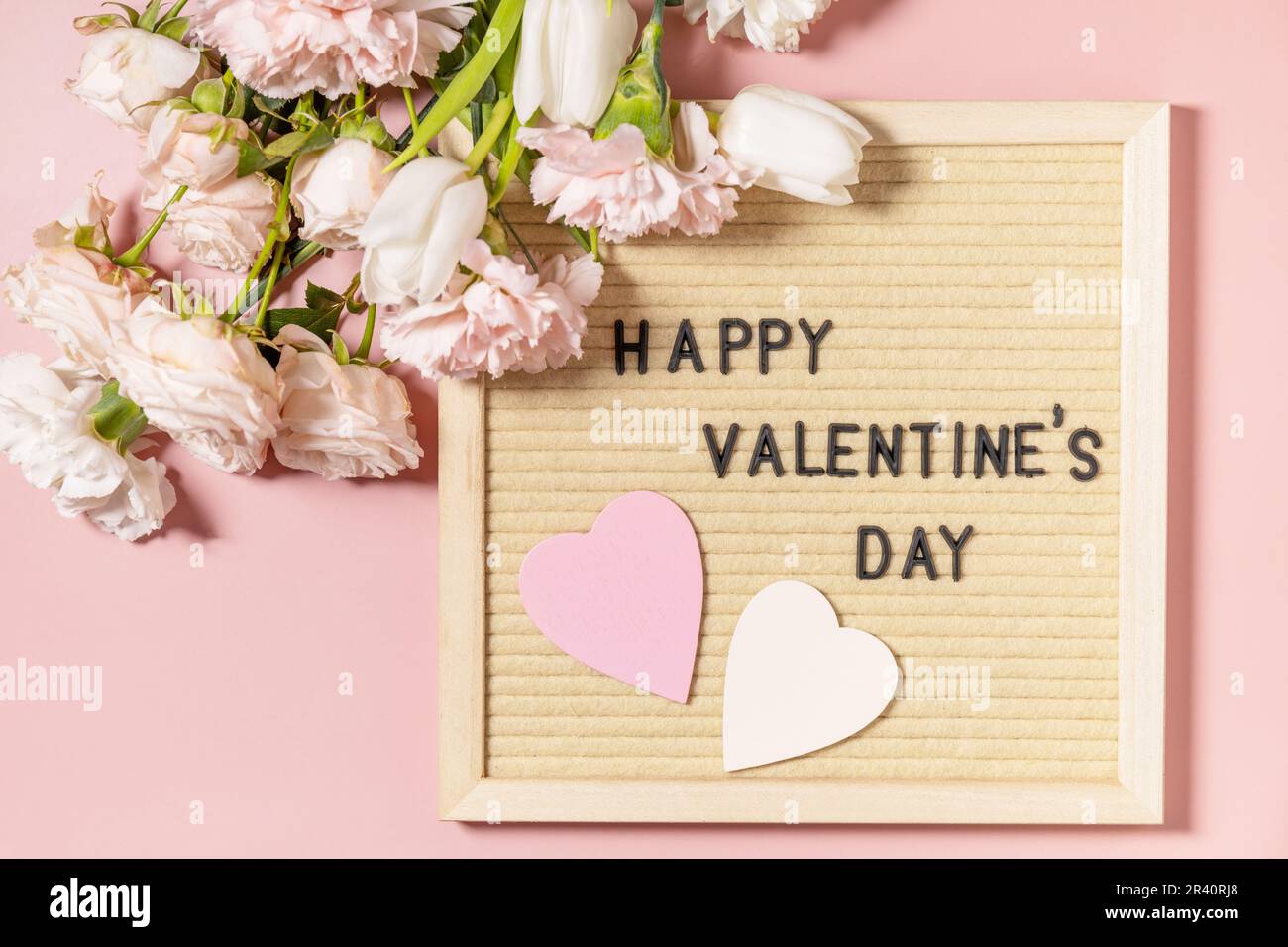 Happy Valentine's Day lettering on letter board and beautiful spring flowers on light pink background. Valentine's day, Womans d Stock Photo