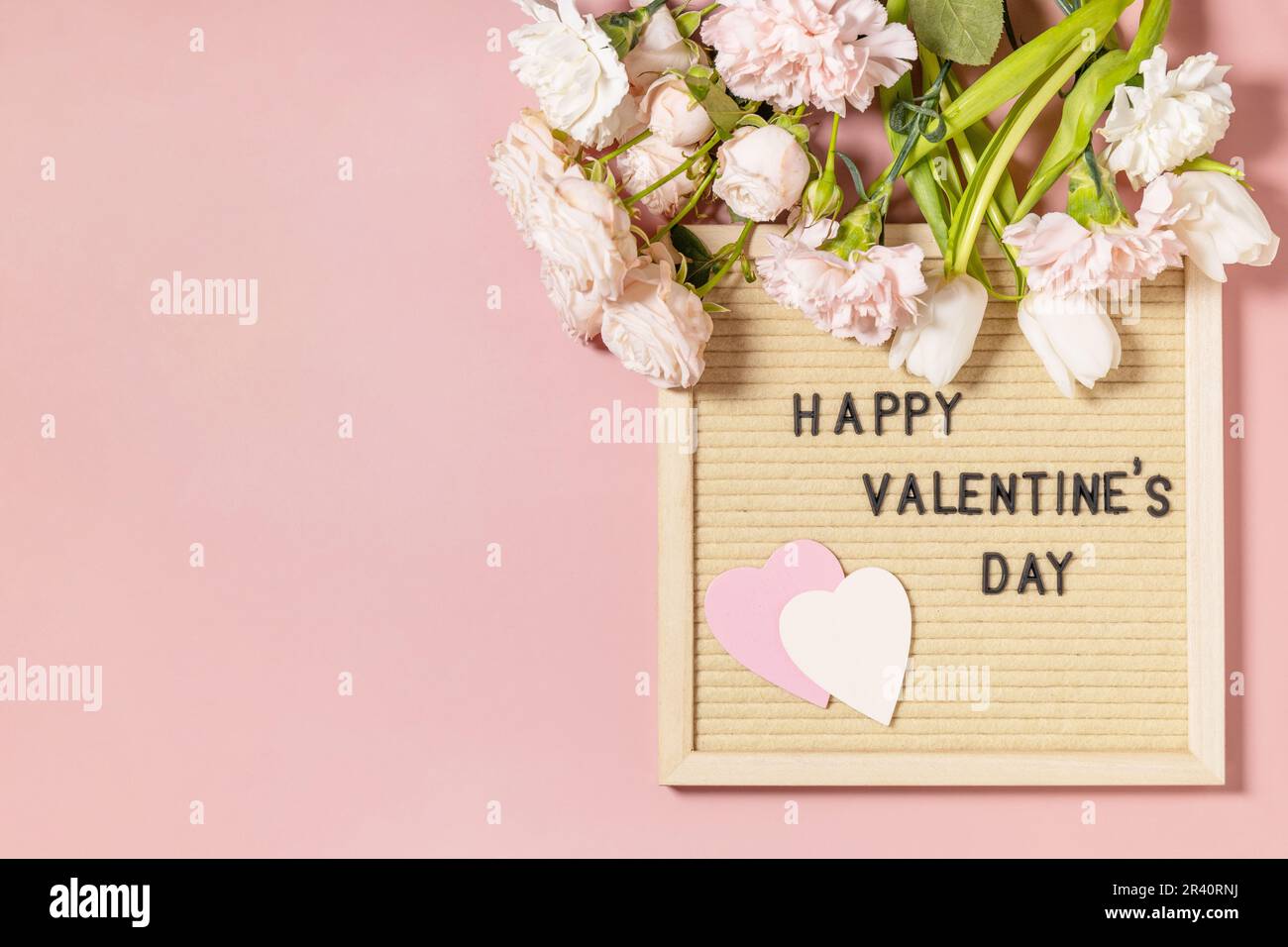 Happy Valentine's Day lettering on letter board and beautiful spring flowers on light pink background. Valentine's day, Womans d Stock Photo