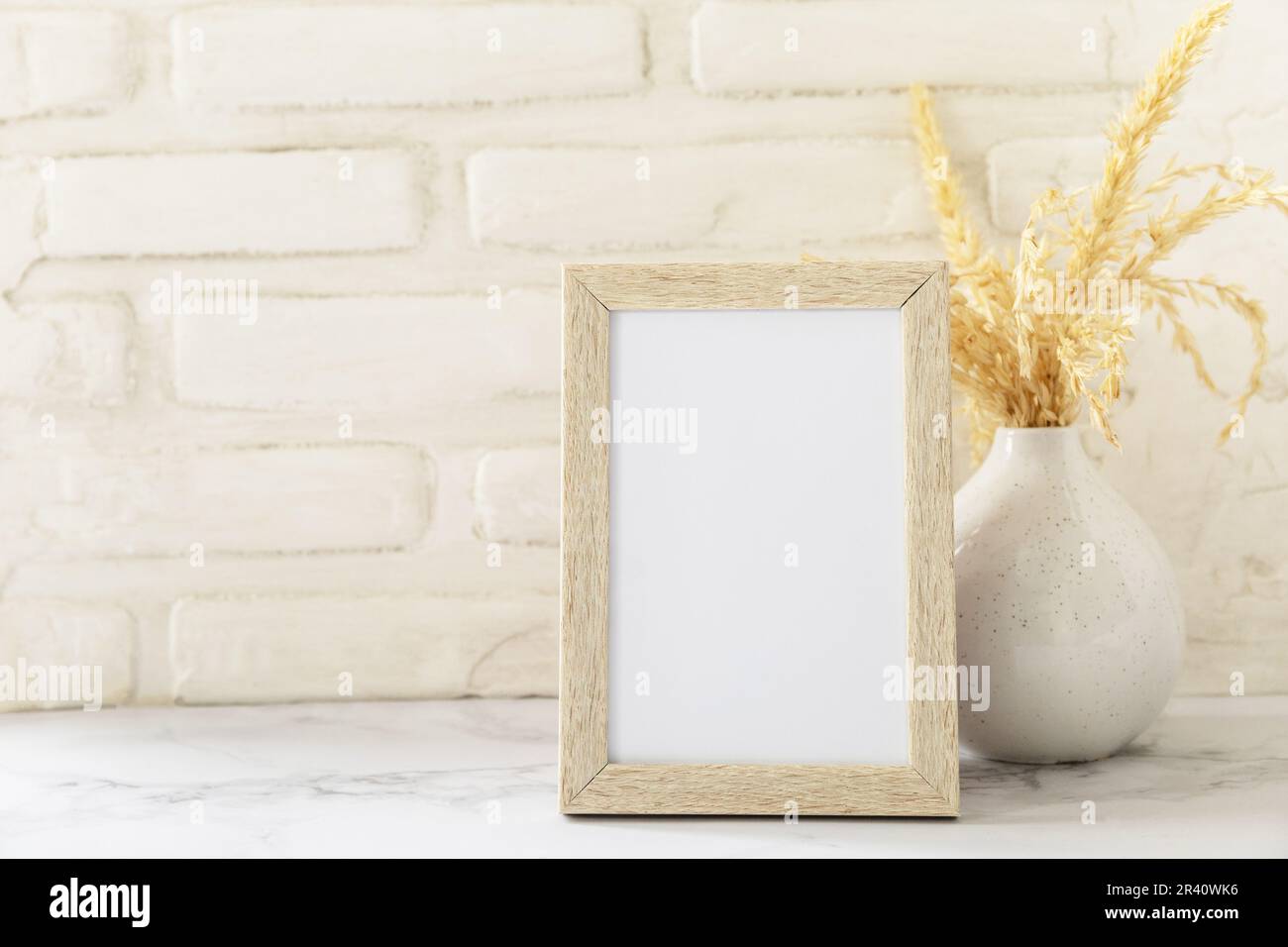 White picture frame mockup. White wall background. Scandinavian interior, neutral color palette with dry grass. Selective focus. Stock Photo