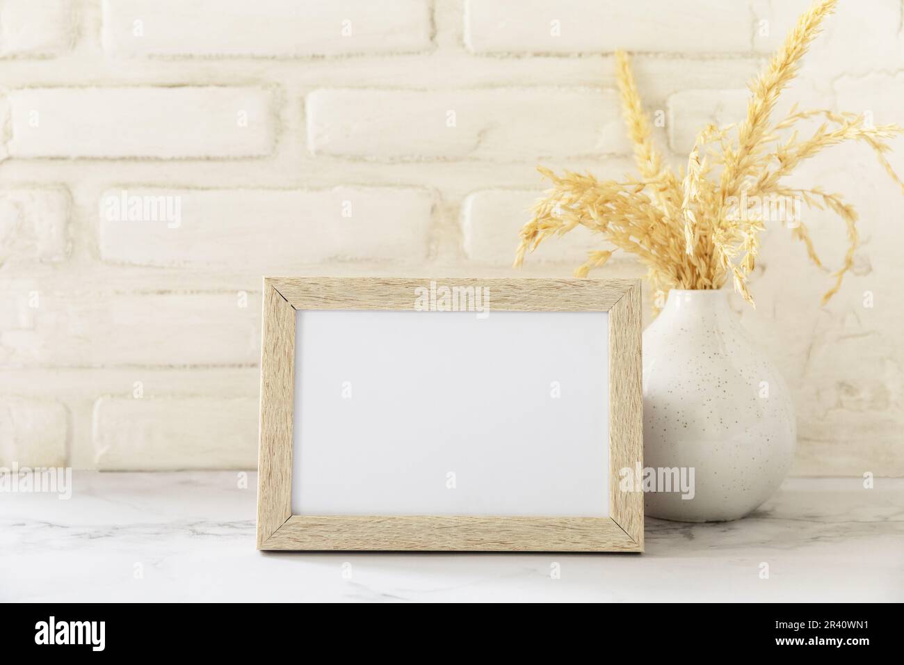 White picture frame mockup. White wall background. Scandinavian interior, neutral color palette with dry grass. Selective focus. Stock Photo