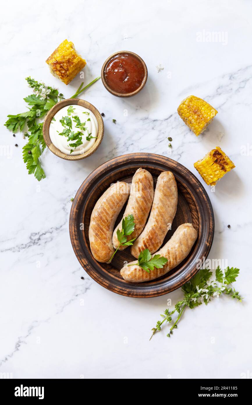 Grill food menu. Summer Party Food. Grilled Sausages with fresh herbs and spices on marble tabletop. View from above. Stock Photo