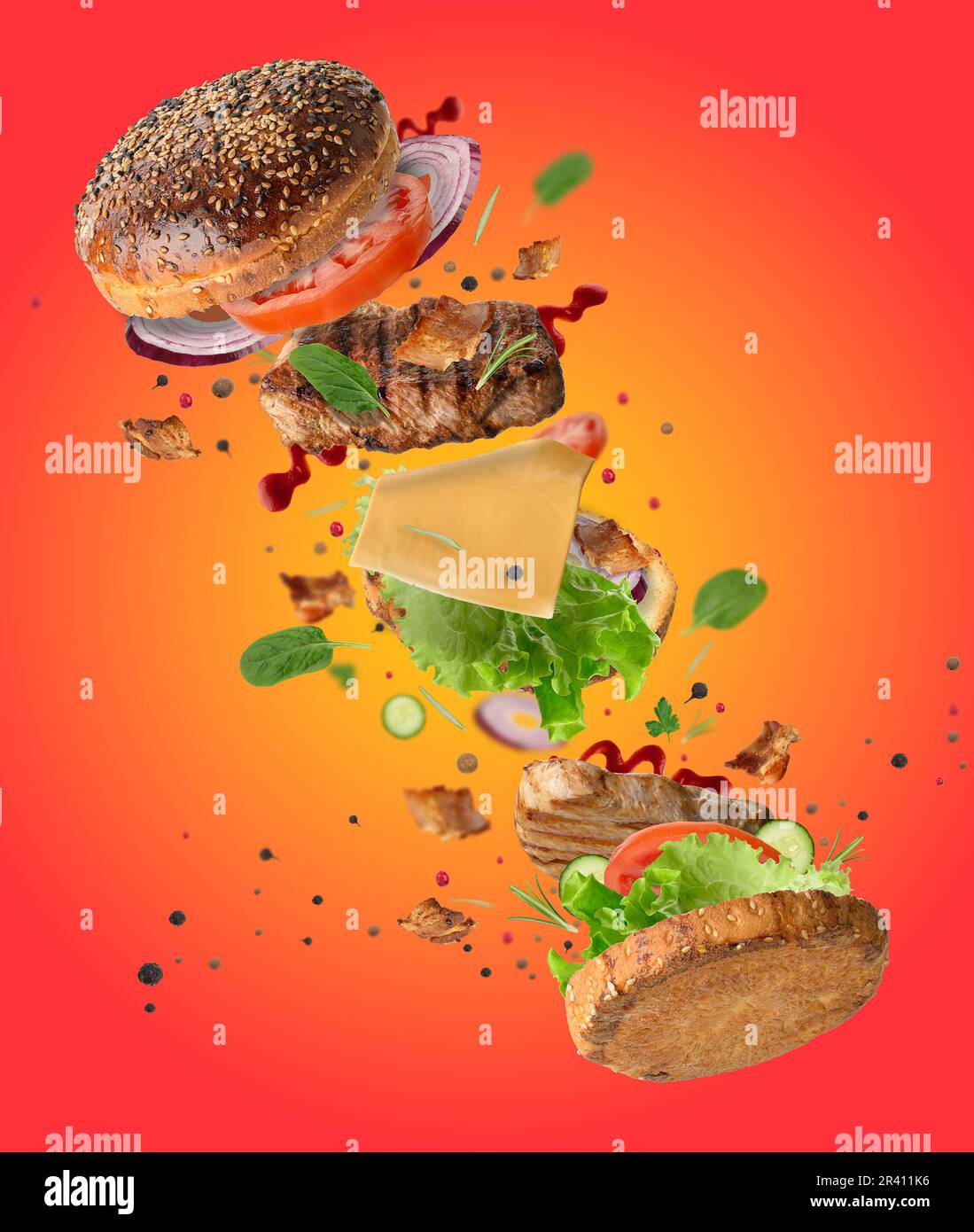 Delicious burger with flying ingredients, pieces of vegetables, spices and meat fried steak on orange background Stock Photo