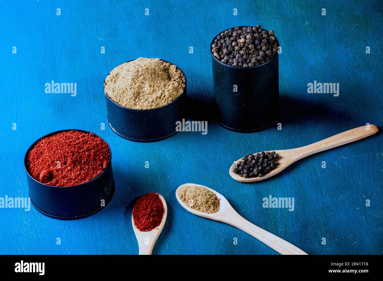 Tin cans and wooden spoons, filled with spices on a hand-painted blue background. With copy space Stock Photo