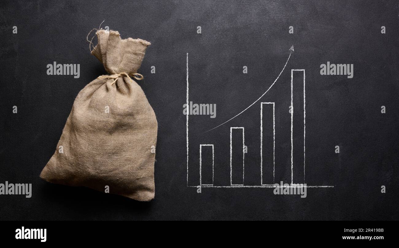 A full canvas bag and a graph drawn in chalk on a black board. Growth of incomes, receipt of subsidies, increase in income Stock Photo